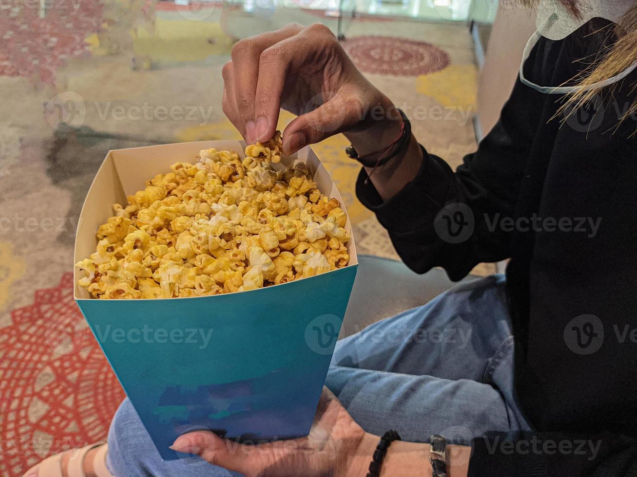 een jong vrouw eet zoet van smaak popcorn terwijl aan het wachten Bij de bioscoop foto