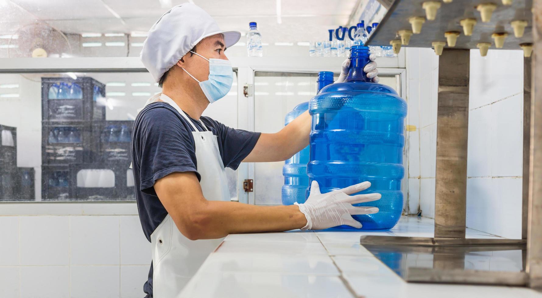 Mens arbeider in werkkleding en met een beschermend masker Aan zijn gezicht werken produceert drinken water in een schoon drinken water fabriek. schoon drinken water productie lijn foto