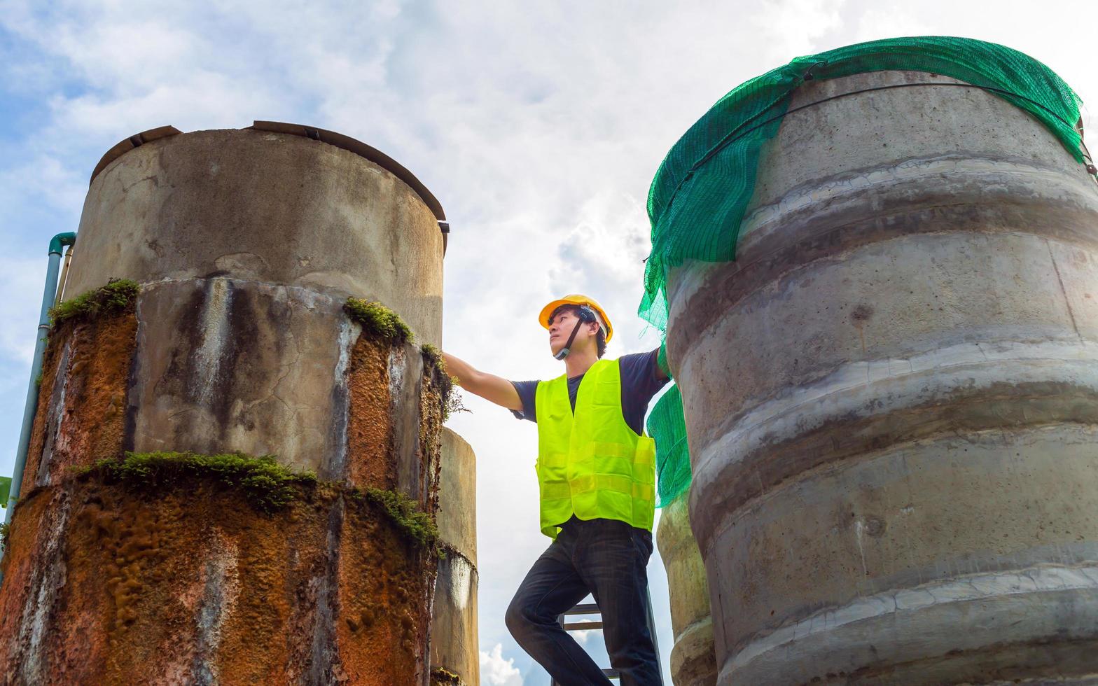 ingenieur controlerend de kwaliteit van water staan Aan de riskant trap Bij hoog plaatsen in werking industrieel water Zuivering of filtratie uitrusting oud cement tanks voor houden water in water fabriek foto