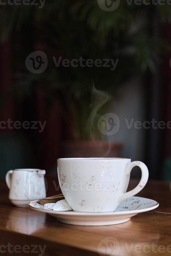 een kop van koffie en een melk kruik Aan een tafel in een oud cafe. foto in wijnoogst kleur, stoom- stijgende lijn van de koffie. verticaal kader, selectief focus. idee voor screensaver of menu, artikel over koffie