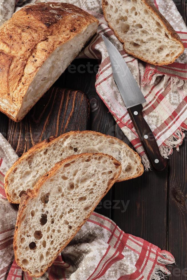 ronde rustiek brood zonder kneden besnoeiing in stukken Aan een snijdend bord Aan een oud donker rustiek tafel. eigengemaakt geheel graan brood, lay-out Aan de tafel, verticaal kader foto