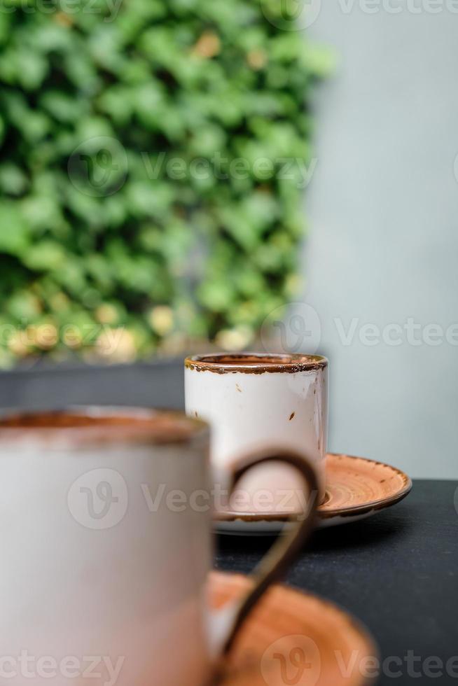 focus Aan de ver kant van de espresso. twee cups van Turks zwart schuimig koffie Aan zwart steen tafel met takken van wild klimop in de achtergrond, bizet De volgende naar de beker. verticaal kader, selectief focus foto