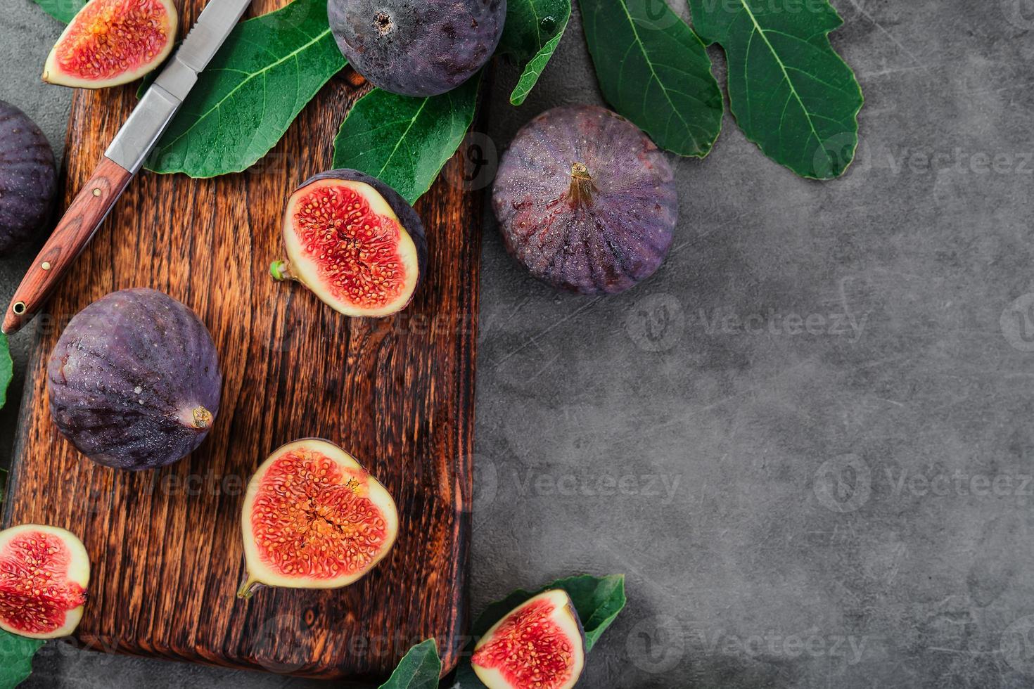 vijgen besnoeiing in plakjes Aan een houten snijdend bord De volgende naar een oud mes. vijgen omringd door fig boom bladeren, gelegd uit Aan grijs keuken tafel. seizoensgebonden rijp fruit, middellandse Zee eetpatroon, idee voor achtergrond foto