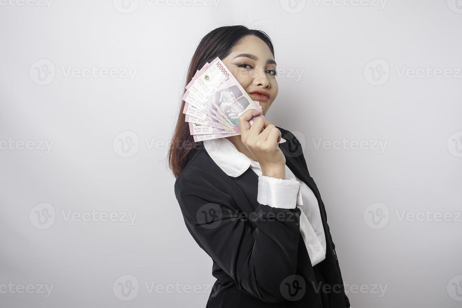 een gelukkig jong zakenvrouw is vervelend zwart pak en Holding contant geld geld in Indonesisch roepia geïsoleerd door wit achtergrond foto