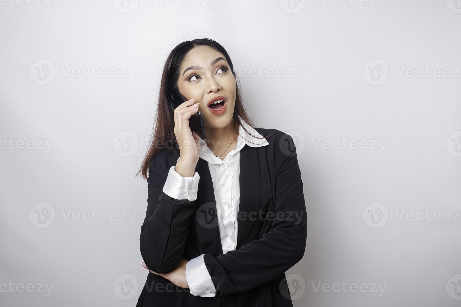 een portret van een gelukkig Aziatisch zakenvrouw is glimlachen terwijl pratend Aan telefoon telefoontje vervelend een zwart pak geïsoleerd door een wit achtergrond foto