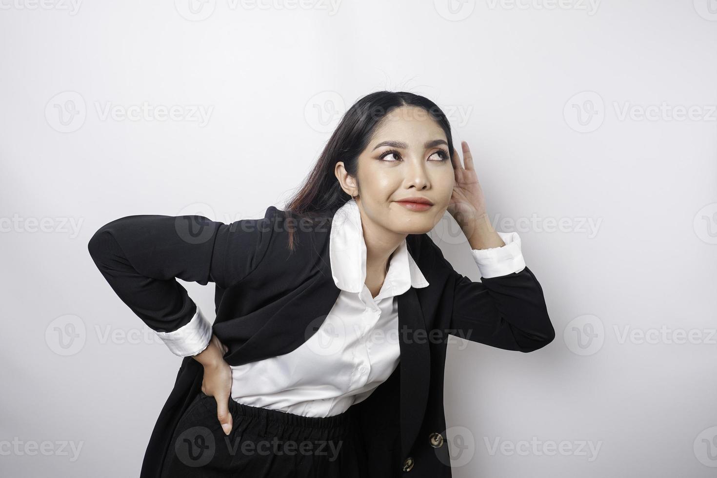 versteld staan nieuwsgierig jong vrouw vervelend een zwart pak proberen naar horen u afluisteren luisteren aandachtig geïsoleerd Aan een wit achtergrond studio portret. foto