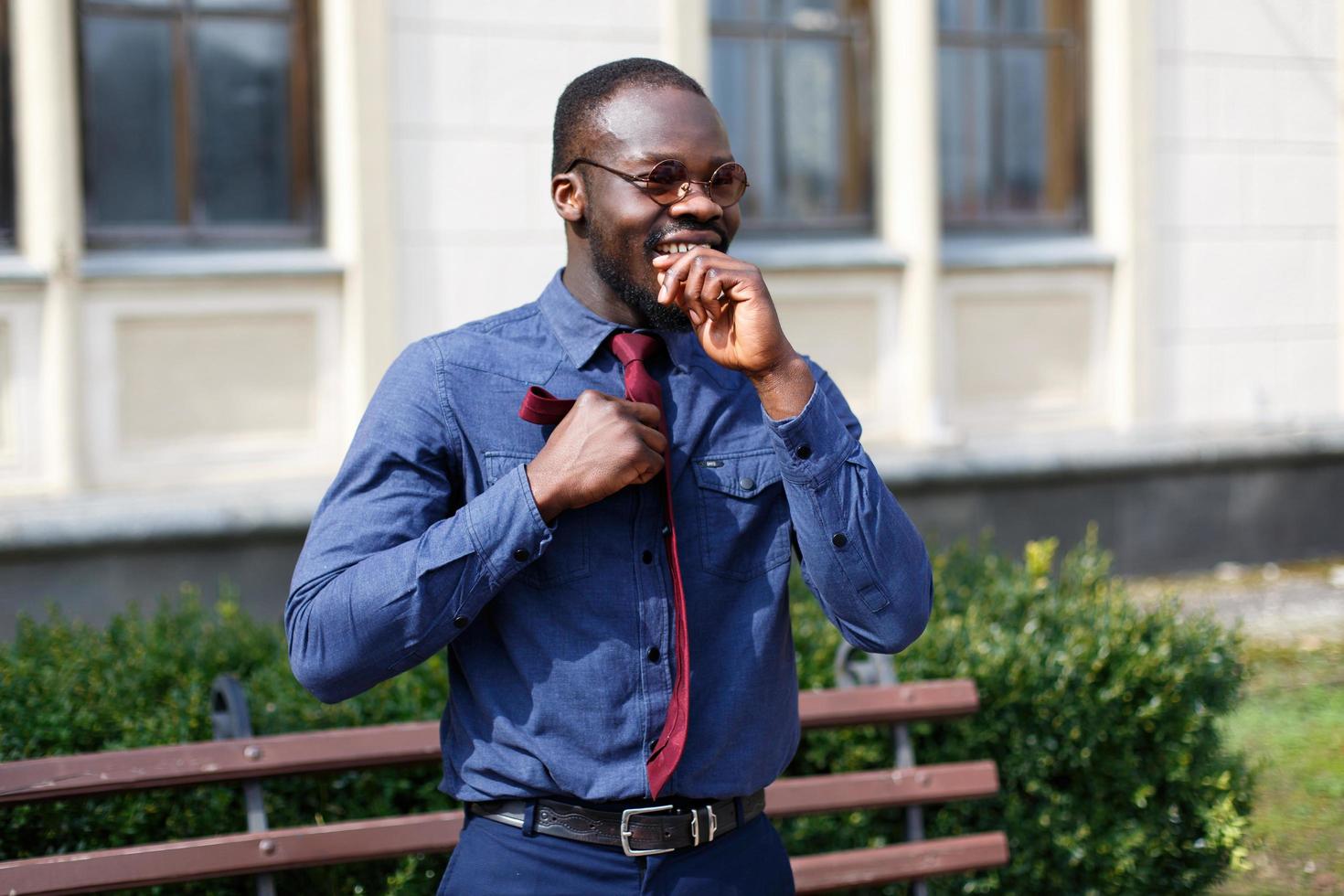 knappe Afro-Amerikaanse man bevestigt zijn rode stropdas op blauw shirt foto