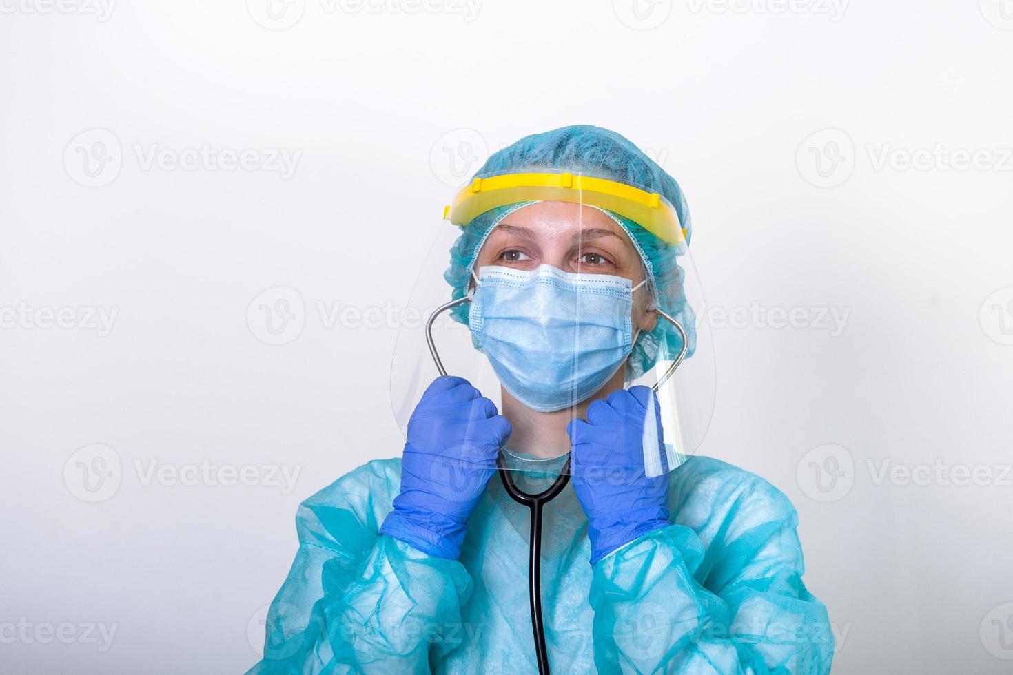 dokter, verpleegster tonen hoe naar vervelend bescherming pak voor vechten covid-19 coronavirus met wit achtergrond geïsoleerd. medisch arbeider in vol beschermend uitrusting met gezicht schild zetten Aan haar stethoscoop foto