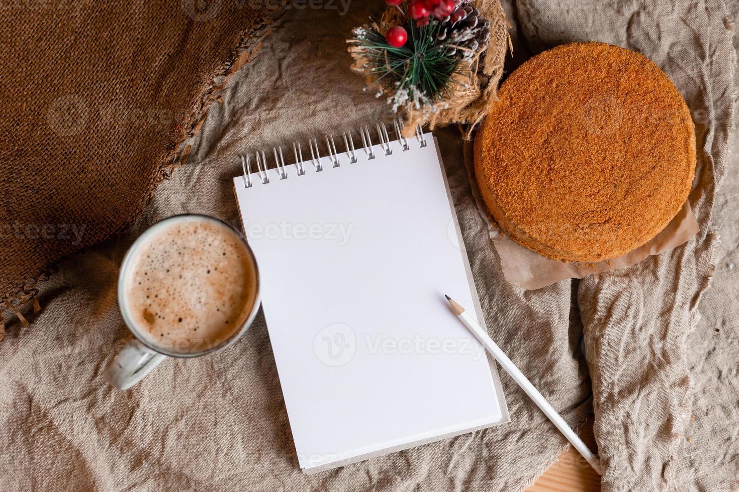 een notitieboekje met leeg Pagina's Aan een houten tafel met koffie en eigengemaakt honing taart. een notitieboekje voor recepten, Koken Bij huis. eigengemaakt taarten, ruimte voor tekst foto