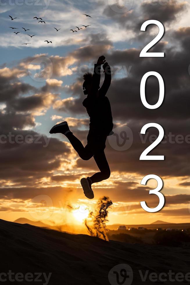 silhouet van Mens jumping met armen omhoog in de zonsondergang met een kudde van vogelstand in de achtergrond. 2023 nieuw jaar concept foto