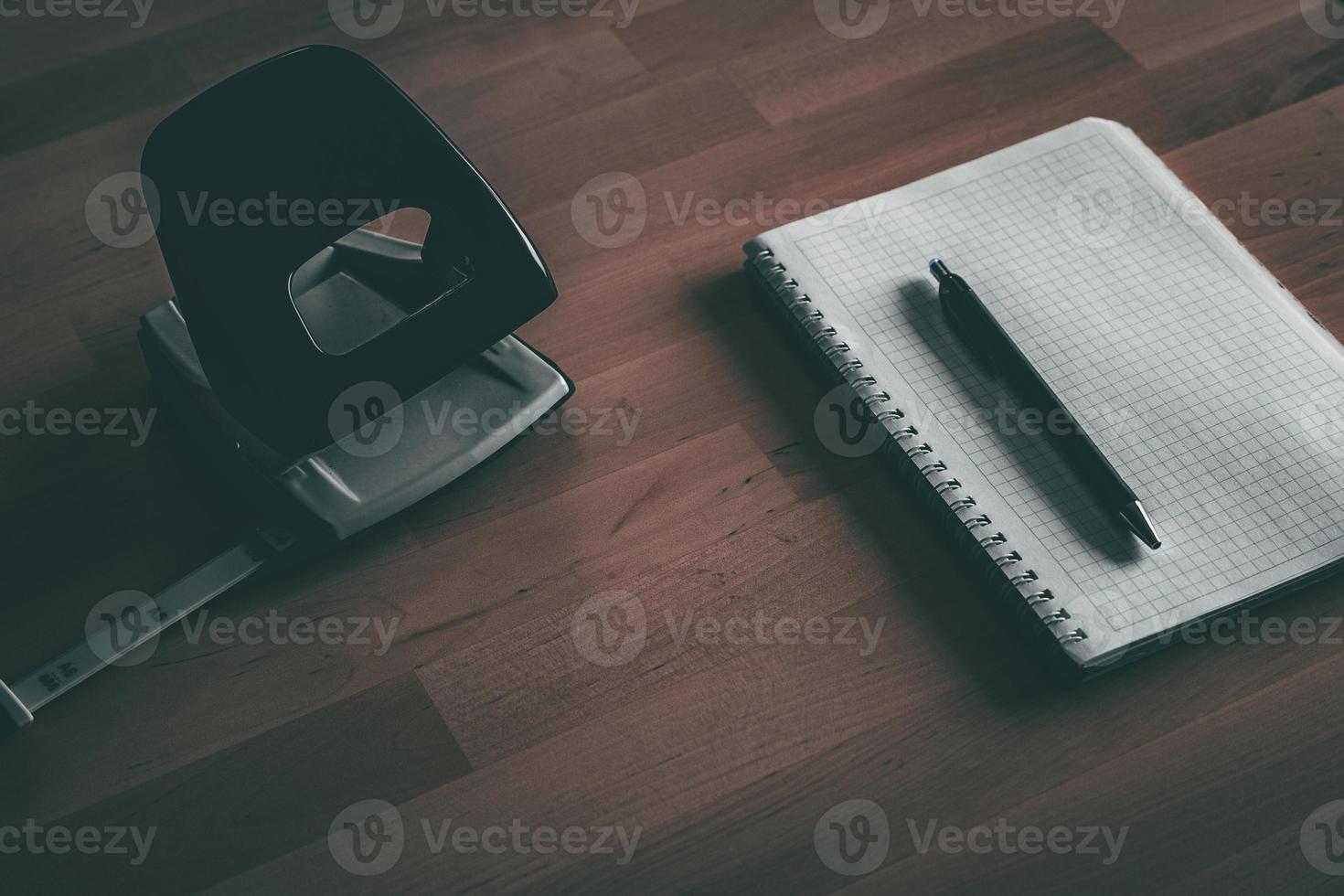 notitieboekje met pen in de buurt papier perforator Aan houten tafel foto