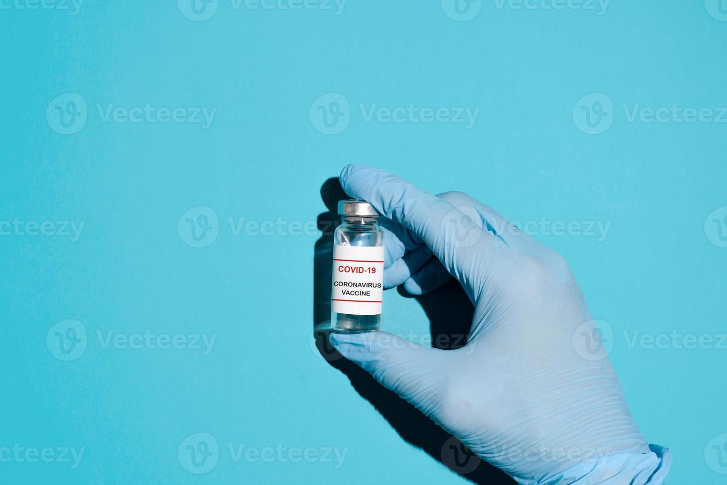 hand- in blauw medisch handschoenen Holding een flacon van covid-19 vaccin Aan een blauw achtergrond, top visie. vaccin productie concept, globaal immunisatie van de bevolking. foto