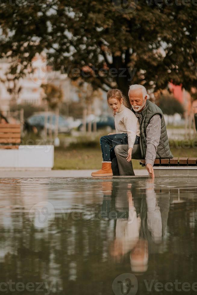 opa uitgeven tijd met zijn kleindochter door klein water zwembad in park Aan herfst dag foto