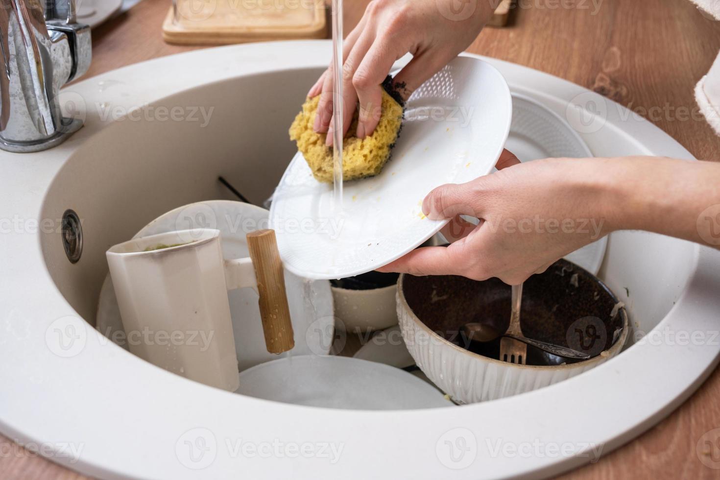 vrouwen handen wassen de bord onder de kraan water. vuil gerechten in de wastafel in de keuken, knoeien na lunch, te lui naar wassen borden. keuken schoonmaak, wasmiddel, schoonmaak Diensten foto