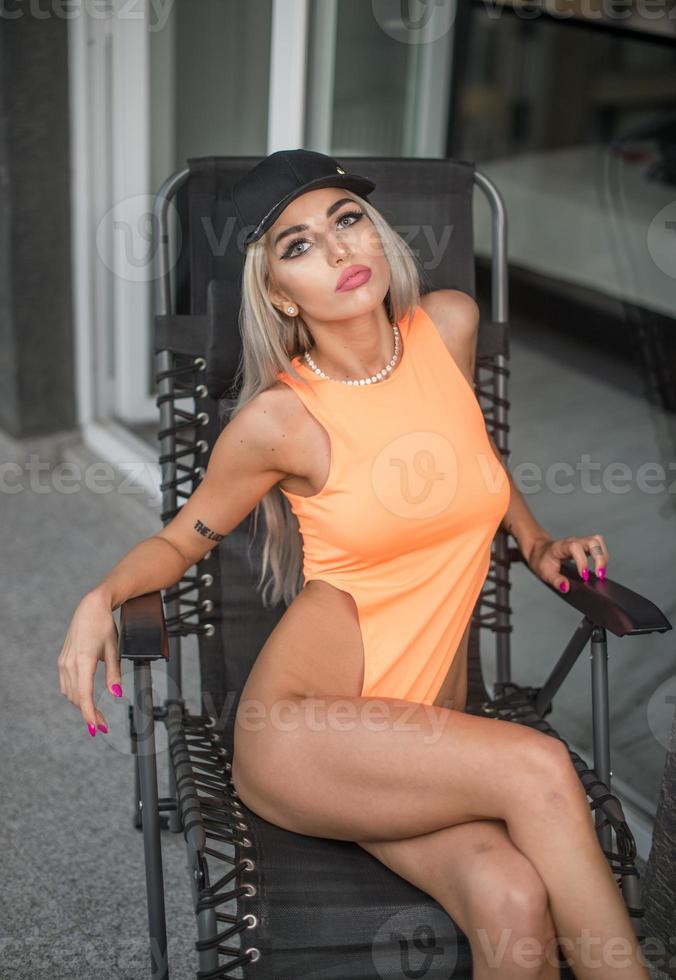 mooi perfect vrouw in oranje bodysuit poseren in voorkant van camera .aantrekkelijk slank blond met perfect gebruind lichaam gesteld in balkon. foto