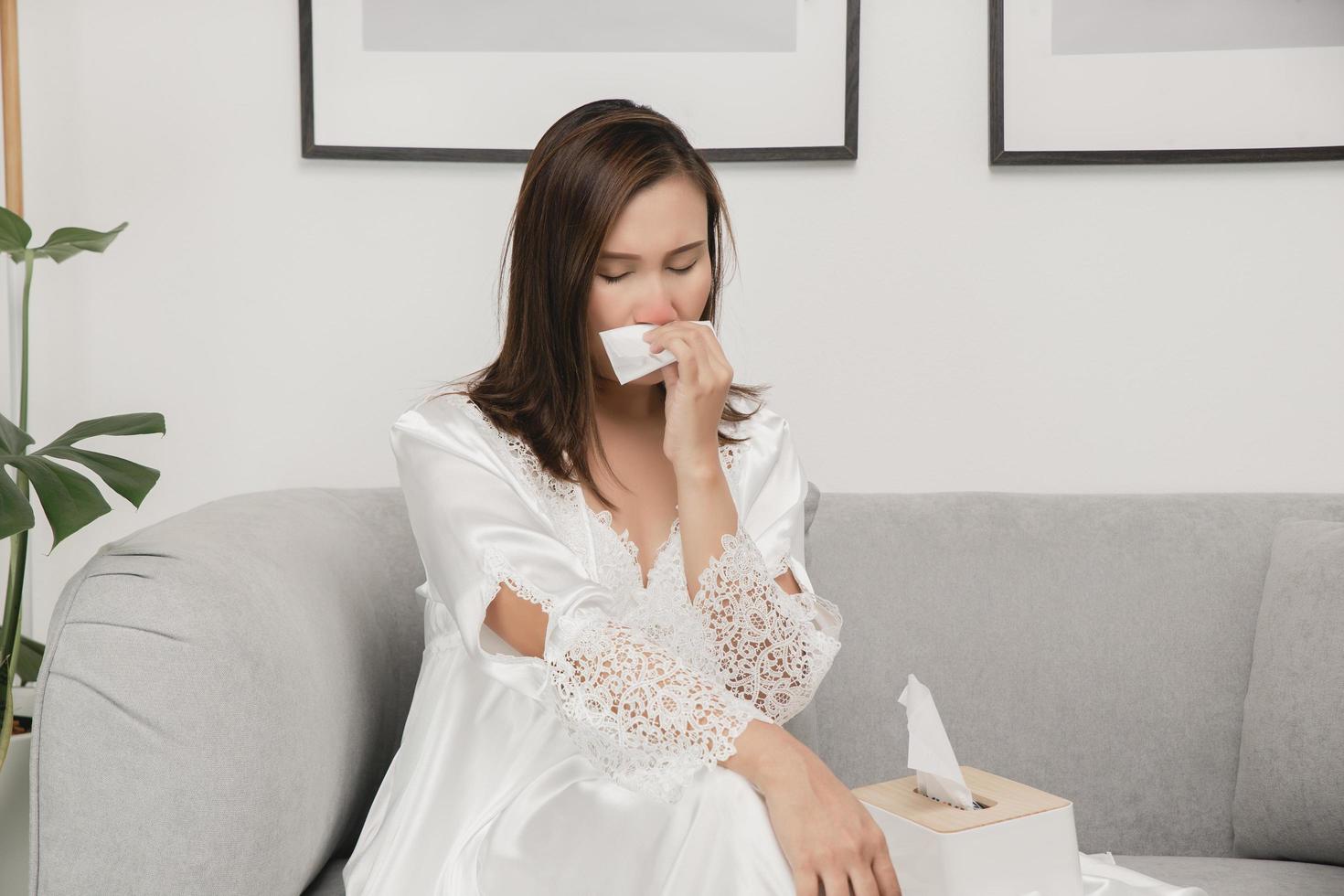 symptomen van allergisch rhinitis in Dames. ziek vrouw in wit nachtkleding met een verkoudheid blazen haar neus- in een zakdoek papier Bij huis. verkoudheid weer allergieën foto