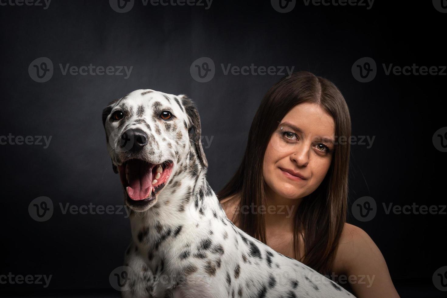 een jong mooi vrouw is spelen met haar dalmatiër huisdier, geïsoleerd Aan een zwart achtergrond. foto