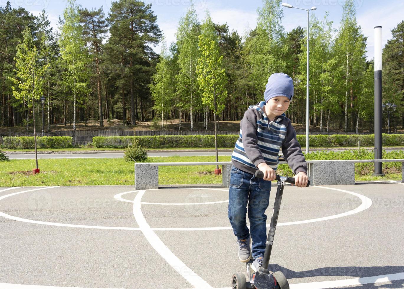 schattig jongen met een scooter hebben pret in de park in de voorjaar foto