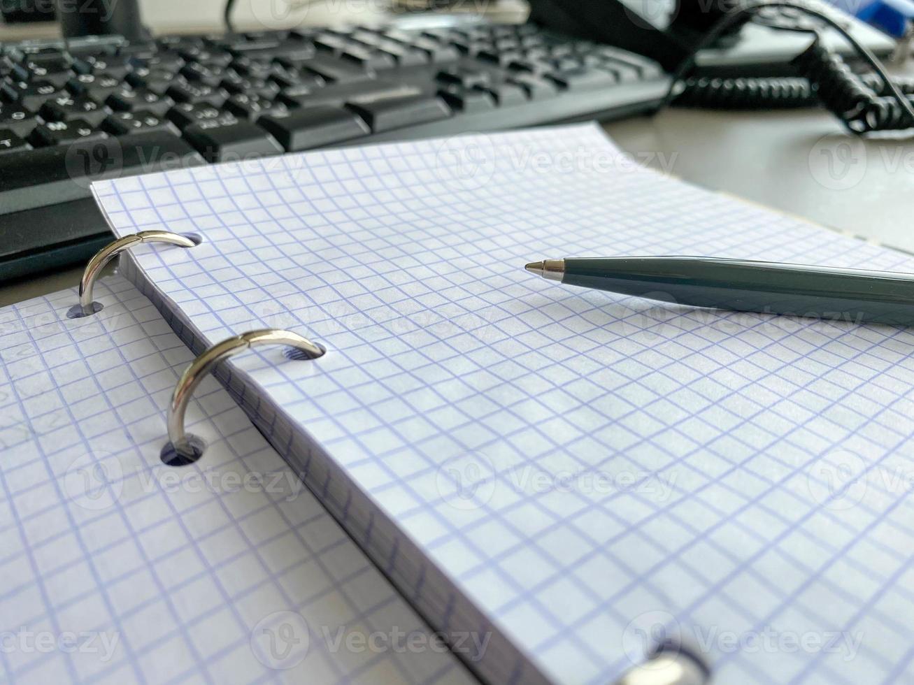 een schrijven pen rust Aan een kladblok met in het kwadraat papier lakens Aan een werk bureau met schrijfbehoeften in een bedrijf kantoor foto