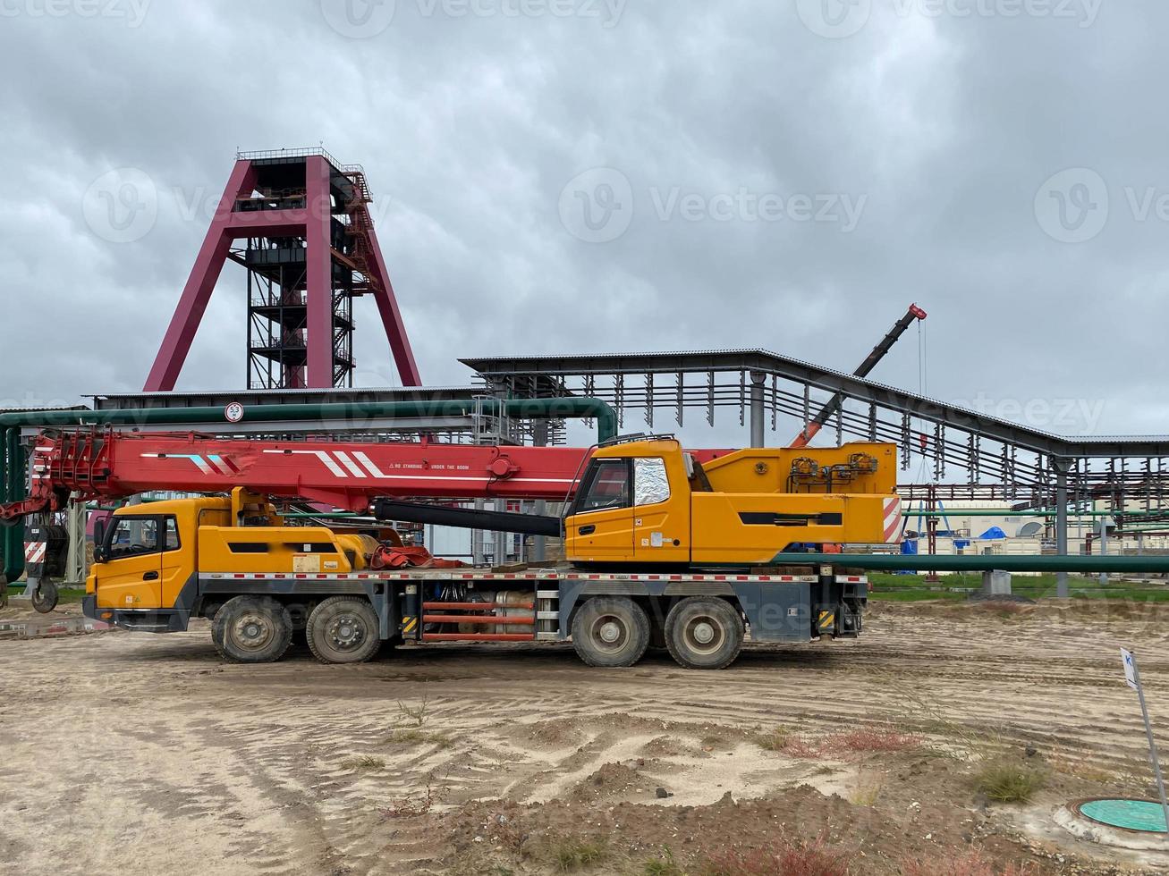 een groot geel vrachtauto kraan staat klaar naar werk Aan de bouw plaats van de nieuw fabriek foto