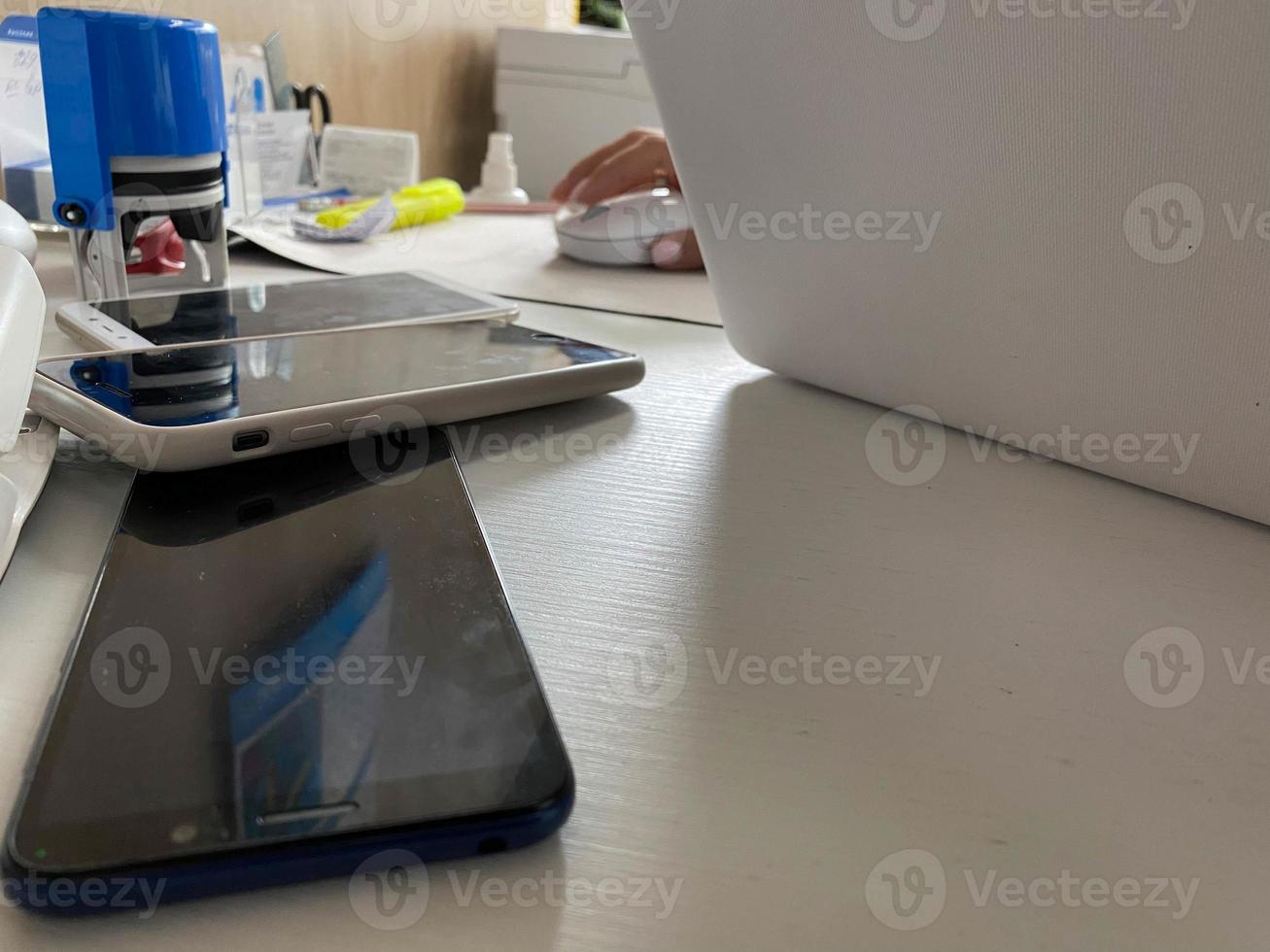 twee werken touch screen mobiel telefoons, smartphones liggen Aan de tafel in de kantoor met briefpapier, een nietmachine, een zegel en een laptop foto