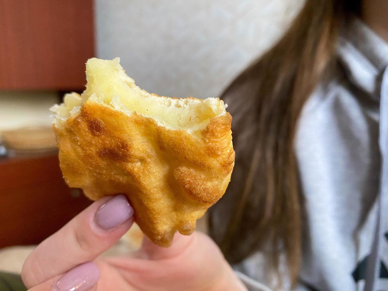 vrouw meisje houdt met haar hand- een gebeten geel heerlijk gebakken pasteitje met aardappelen foto