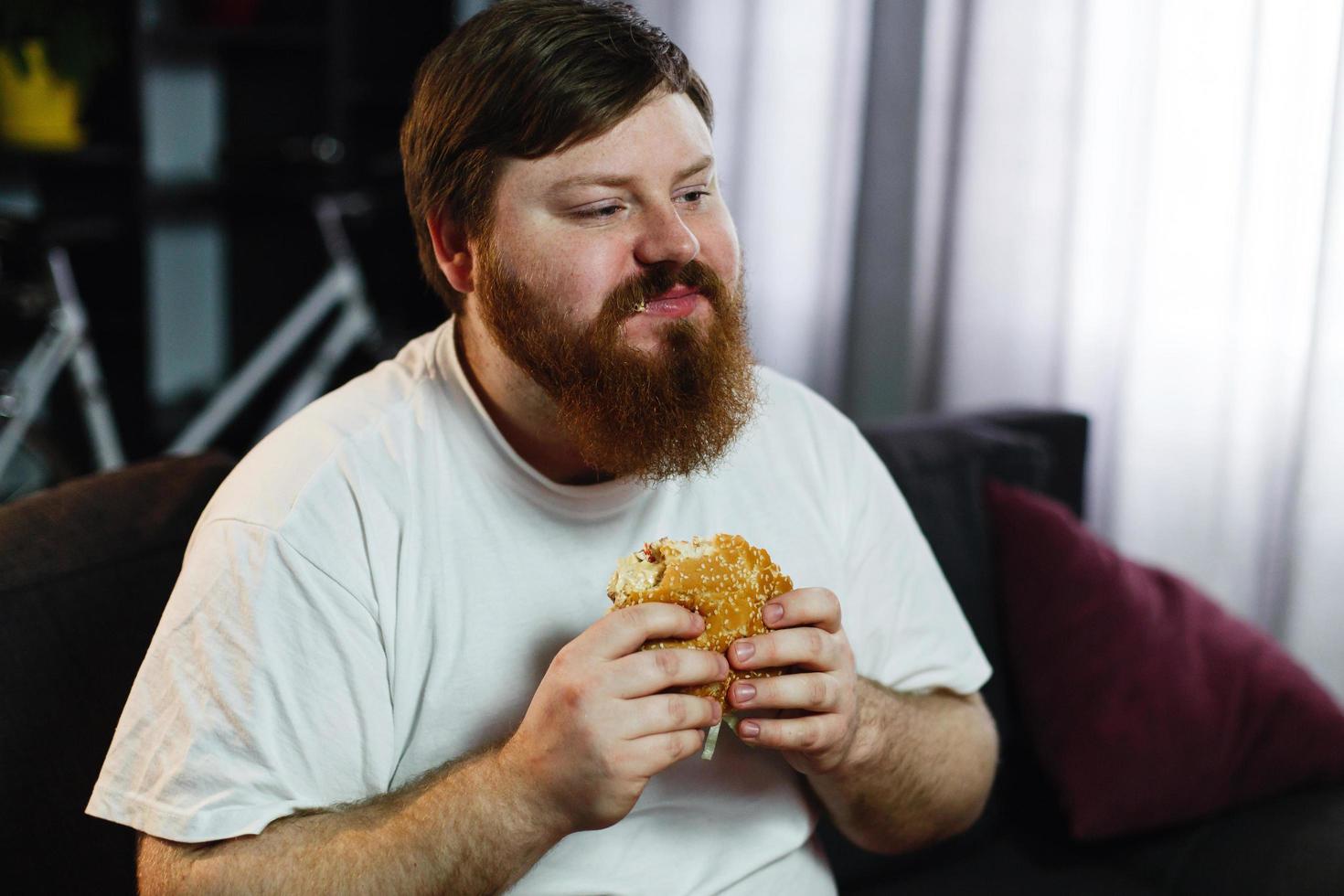 man eet een hamburger terwijl hij tv kijkt foto