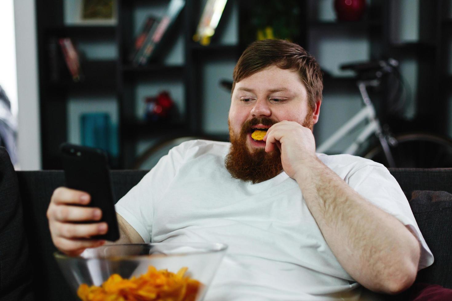 man controleert zijn smartphone terwijl hij op de bank zit en eet foto