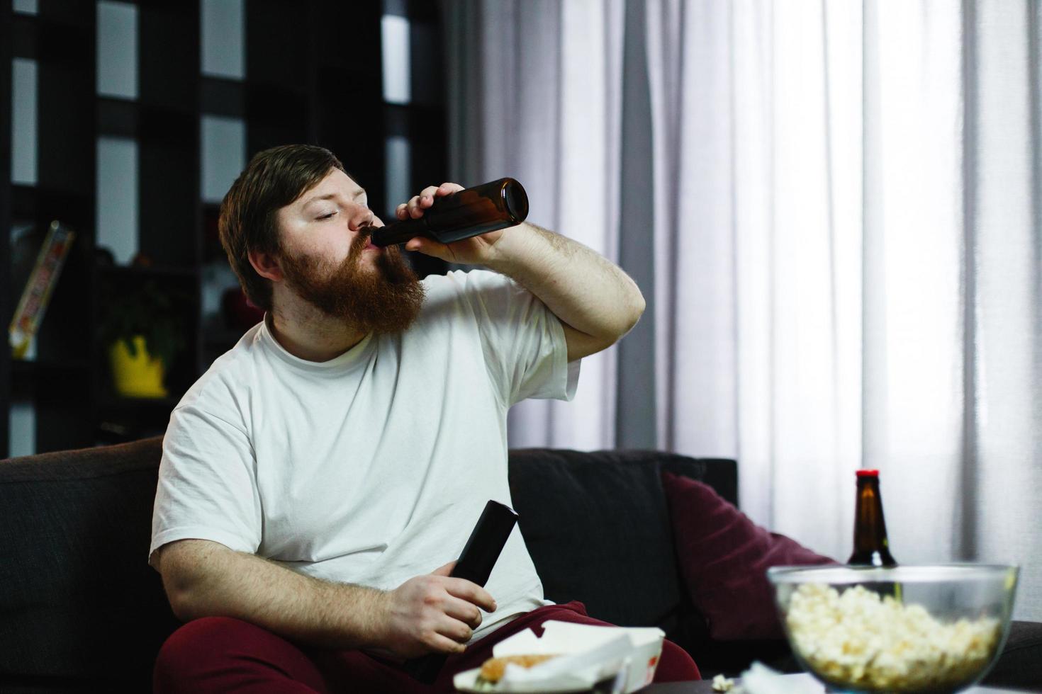 dikke man drinkt bier liggend op de bank foto