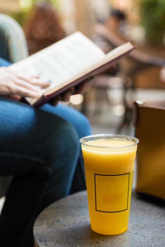 vrouw lezen van een boek met oranje cocktail in café foto