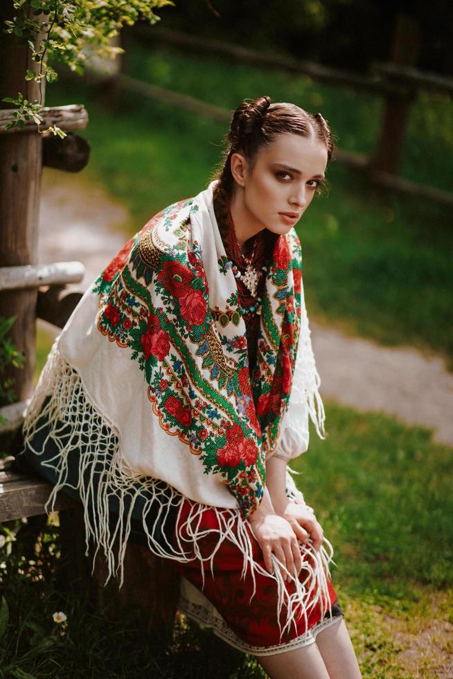 jong meisje in een traditionele Oekraïense jurk zit op een bankje in het park foto