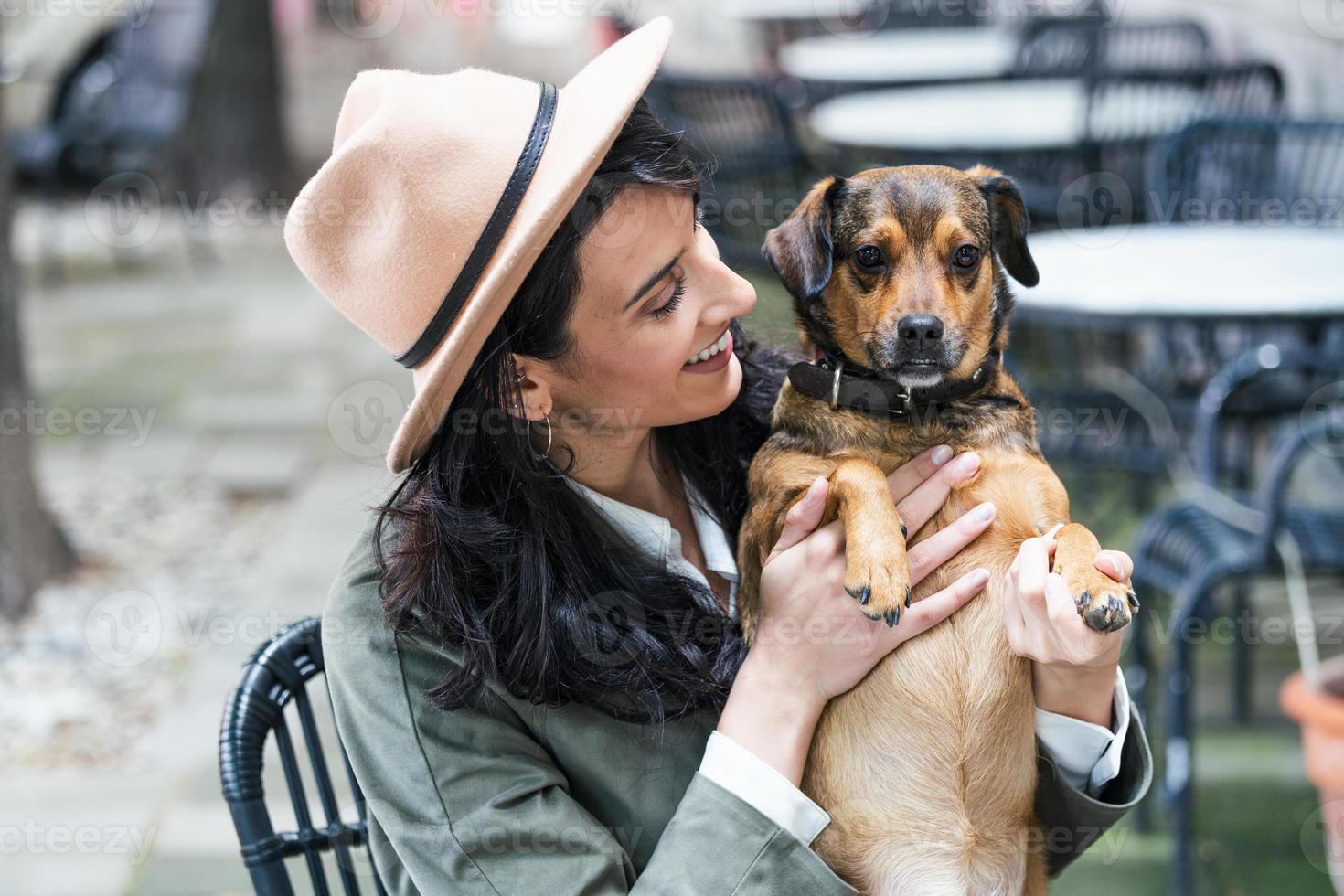 aantrekkelijk jong vrouw zittend in koffie winkel, ontspannende en Holding haar hond. huisdier vriendelijk cafetaria, mooi meisje met haar hond locatie Bij een koffie winkel en drinken koffie. foto