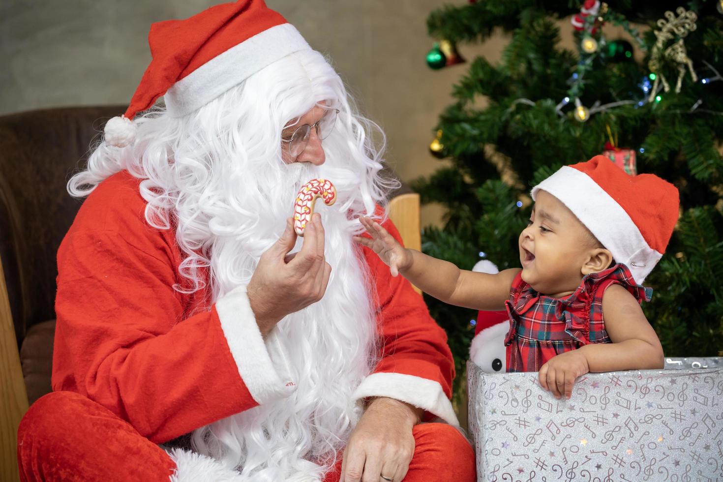 Afrikaanse Amerikaans baby is krijgen koekje net zo Cadeau van de kerstman claus Bij nacht door de ten volle versierd Kerstmis boom voor seizoen viering concept foto