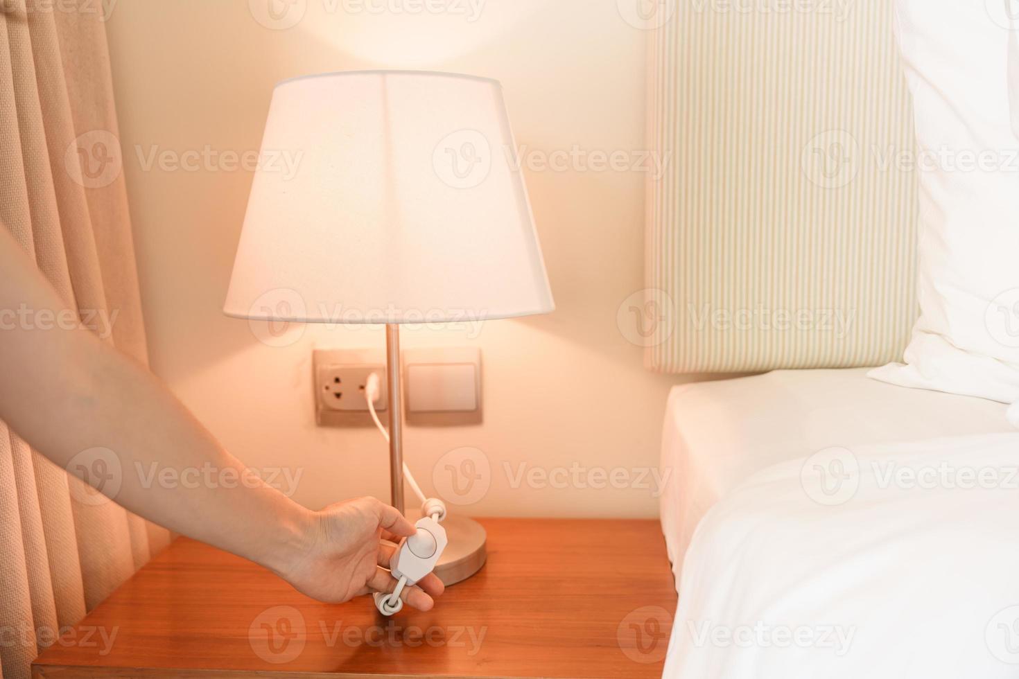 vrouw hand- draaien Aan of draaien uit schakelaar de minimaal lamp in modern slaapkamer. appartement leven concept foto