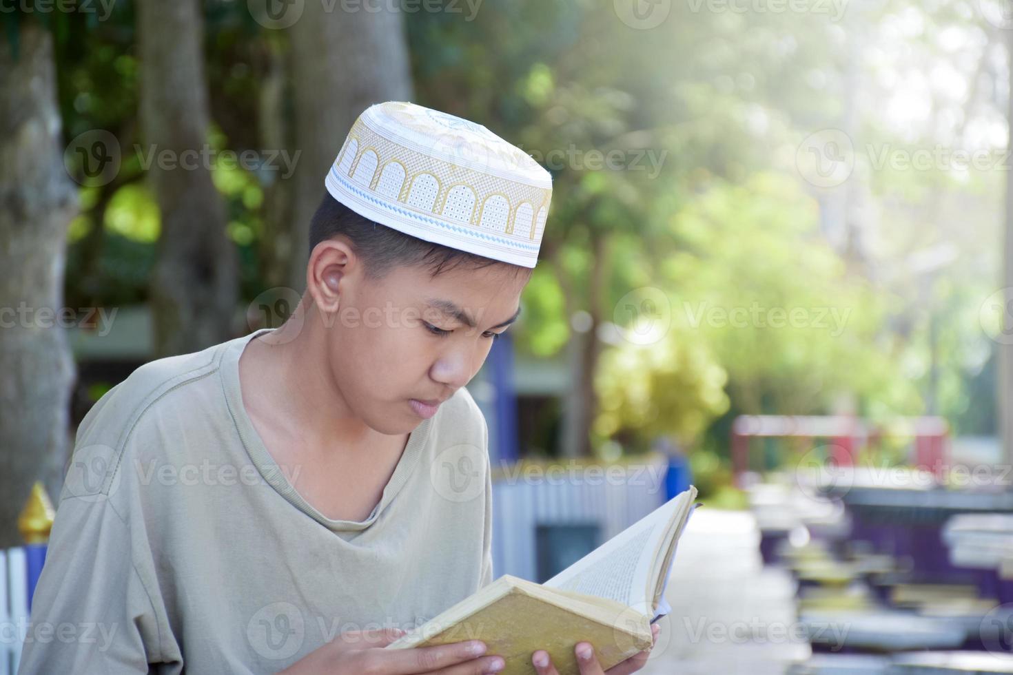 jong Aziatisch moslim jongen draagt hoed, zittend in school- park en lezing zijn boek in zijn vrij keer voordat gaan terug huis, zacht en selectief focus. foto