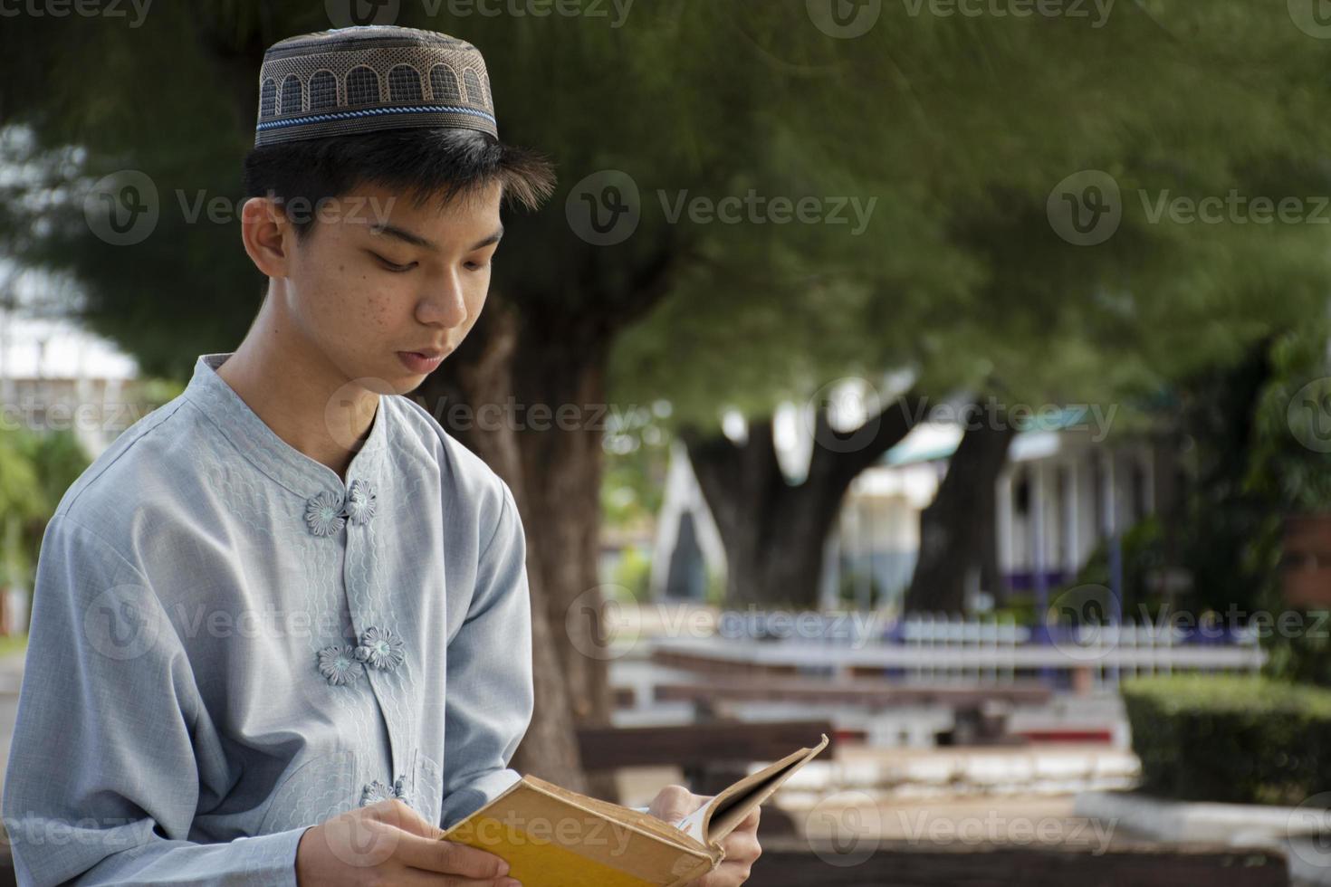 jong Aziatisch moslim jongen draagt hoed, zittend in school- park en lezing zijn boek in zijn vrij keer voordat gaan terug huis, zacht en selectief focus. foto