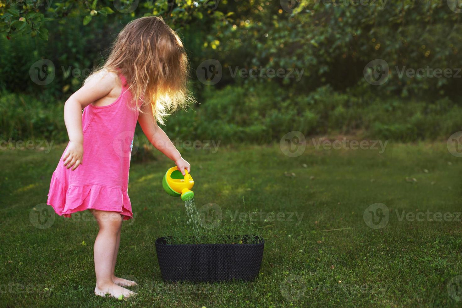 schattig weinig meisje gieter bloemen in de zomer tuin foto