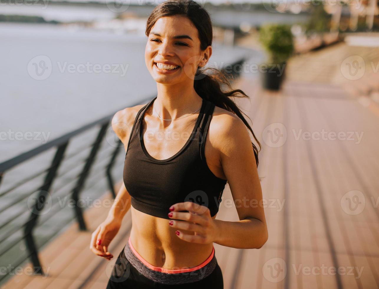 actief jong mooi vrouw rennen Aan de promenade langs de rivieroever foto