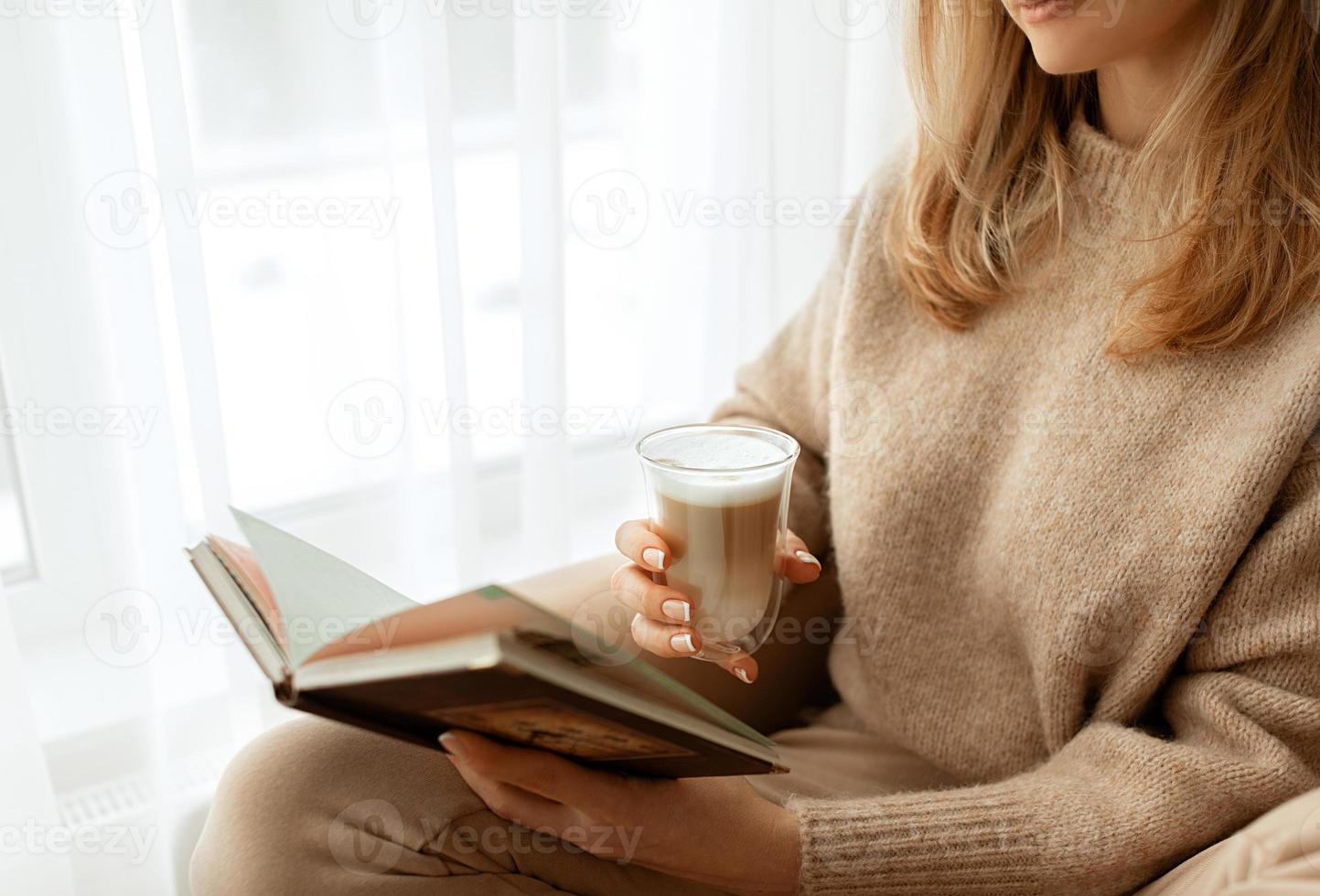 dichtbij omhoog vrouwen handen en vingers met een mooi Frans manicure Holding kop transparant glas met koffie met wit schuim.kopie ruimte voor tekst, spandoek. beige gebreid trui en achtergrond. foto