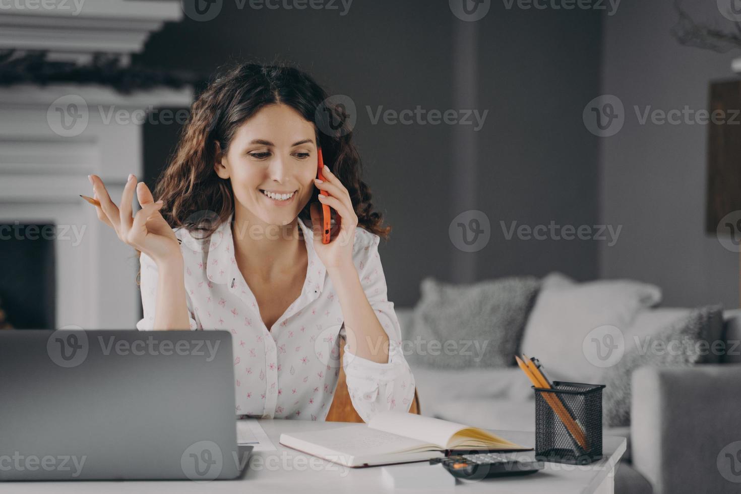 gelukkige Spaanse zakenvrouw met mobiele telefoon, bellen tijdens thuiswerk op afstand foto