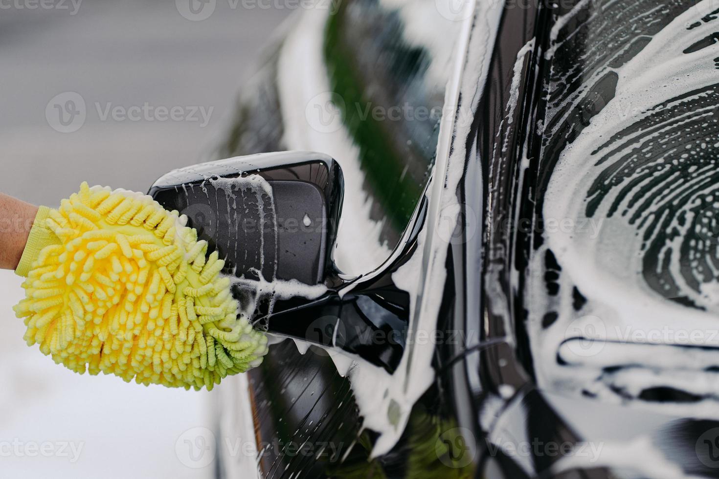 onherkenbare man wast zwarte auto met doek of lap want, gebruikt speciaal wasmiddel. vuile auto schoonmaken. carwash bedrijfsconcept. foto