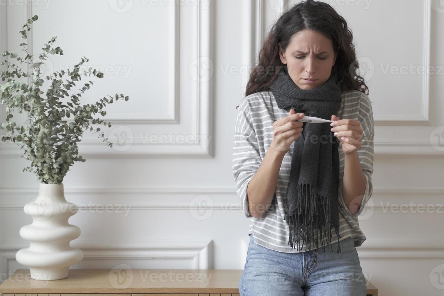 ongezonde zieke jonge italiaanse vrouw die een thermometer vasthoudt en thuis hoge temperaturen meet foto