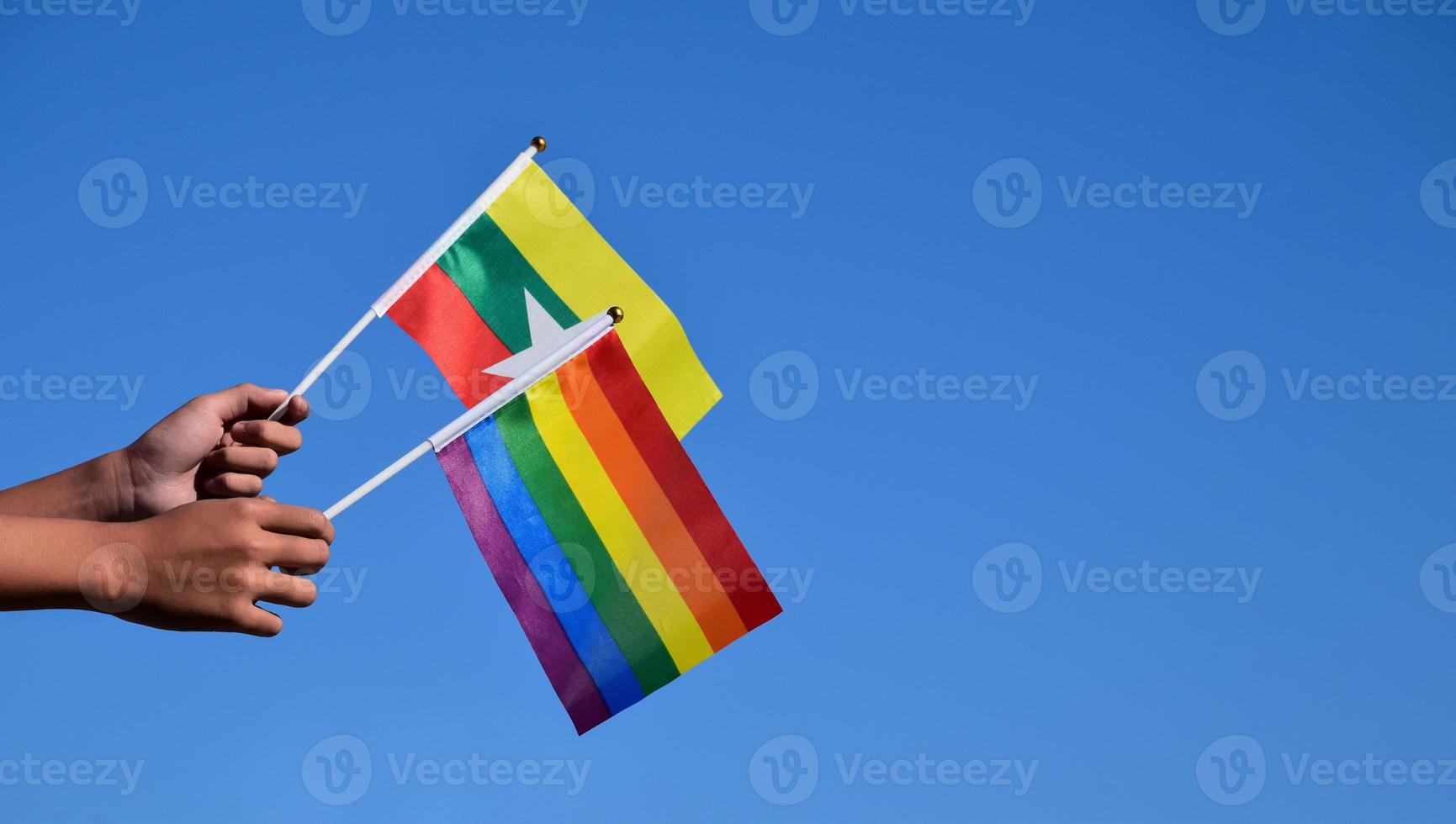 Myanmar en regenboog vlaggen, lgbt symbool, Holding in handen, blauwe lucht achtergrond, concept voor lgbt viering in Myanmar en in de omgeving van de wereld in trots maand, juni, zacht en selectief focus, kopiëren ruimte. foto