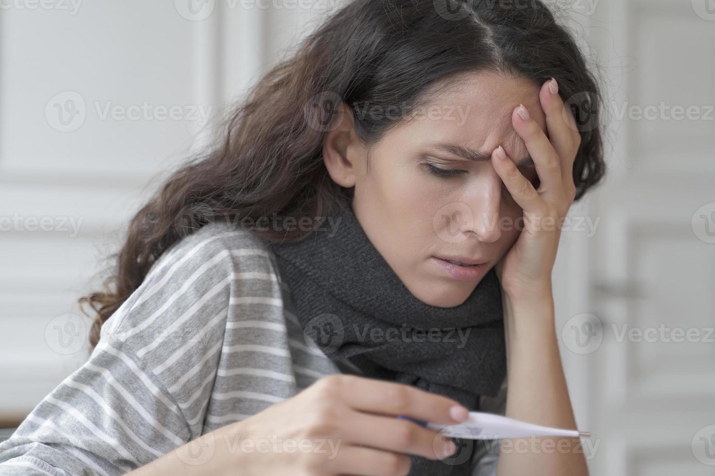 zieke zieke Spaanse vrouw met hoofdpijn die thuis de temperatuur meet foto