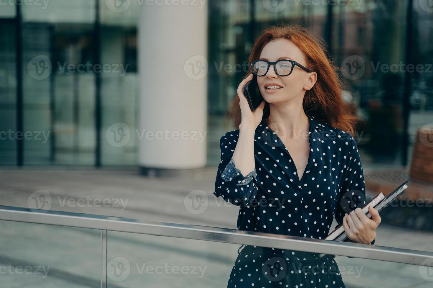 nadenkende roodharige vrouw draagt bril polka dot jurk heeft telefoongesprek foto