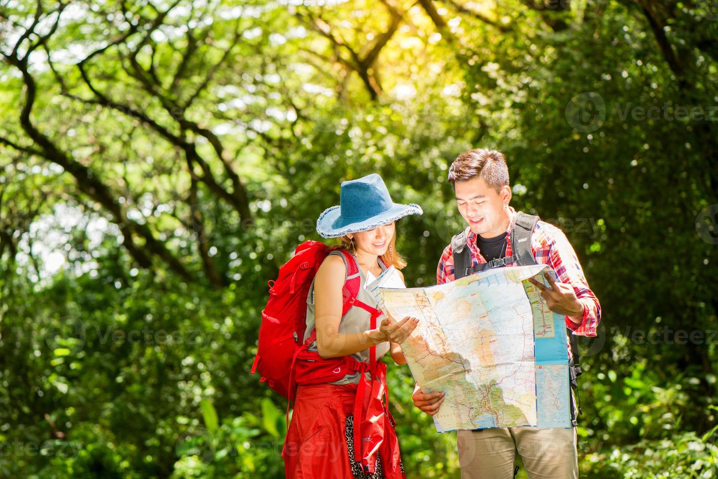 wandelen - wandelaars op zoek Bij kaart. paar of vrienden navigeren samen glimlachen gelukkig gedurende camping reizen wandeltocht buitenshuis in Woud. jong gemengd ras Aziatisch vrouw en Mens. foto