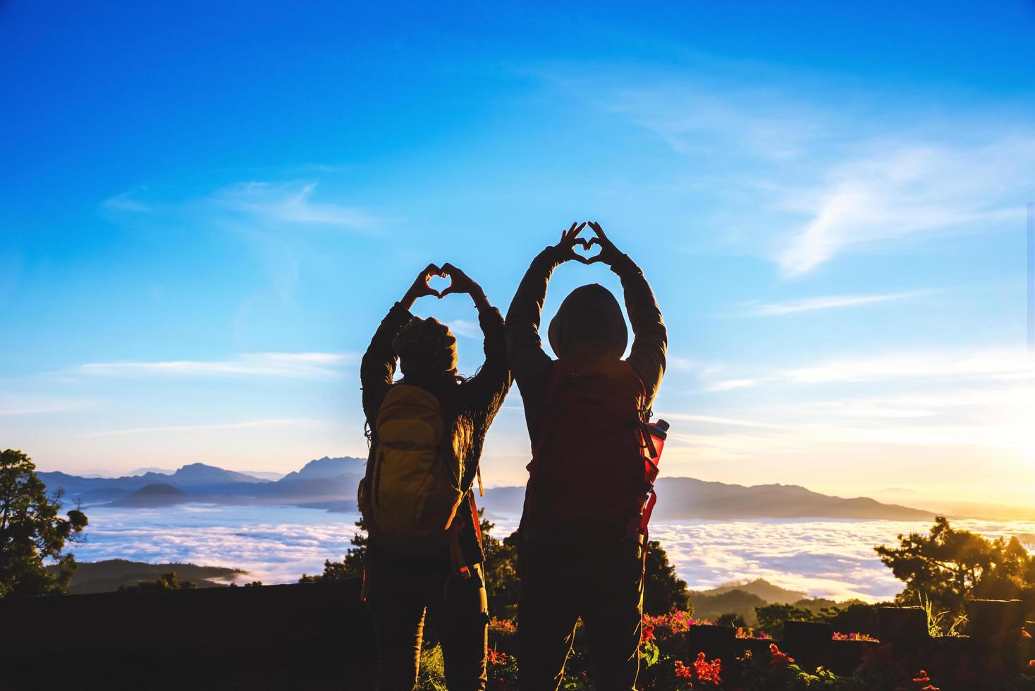 minnaar vrouwen en mannen aziaten reizen ontspannen in de vakantie. sta op voor zonsopgang op de berg, gelukkige huwelijksreis, hief zijn hand op om een hartvorm te maken. foto