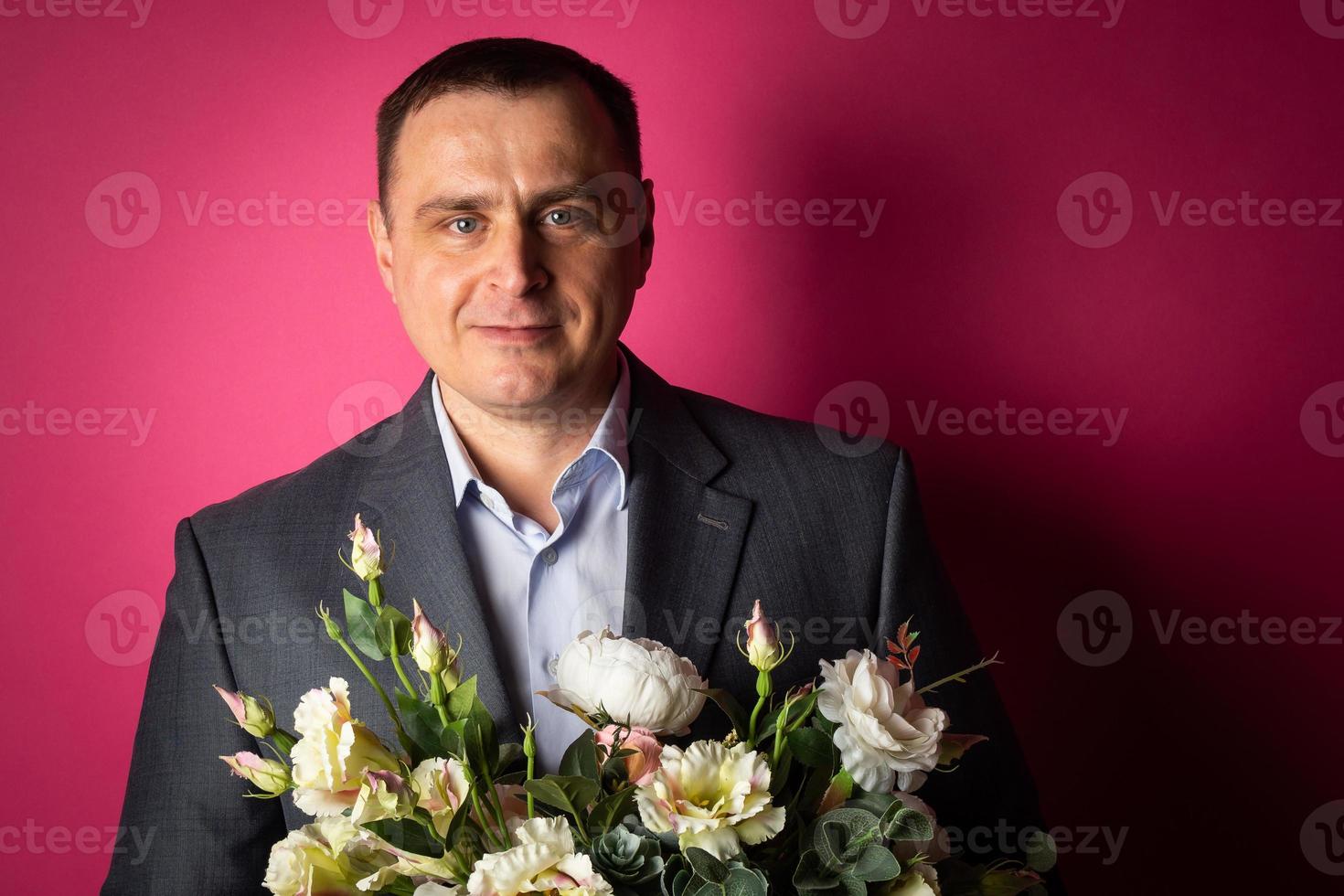 knap zakenman in een pak looks Bij de camera met een boeket van bloemen. foto