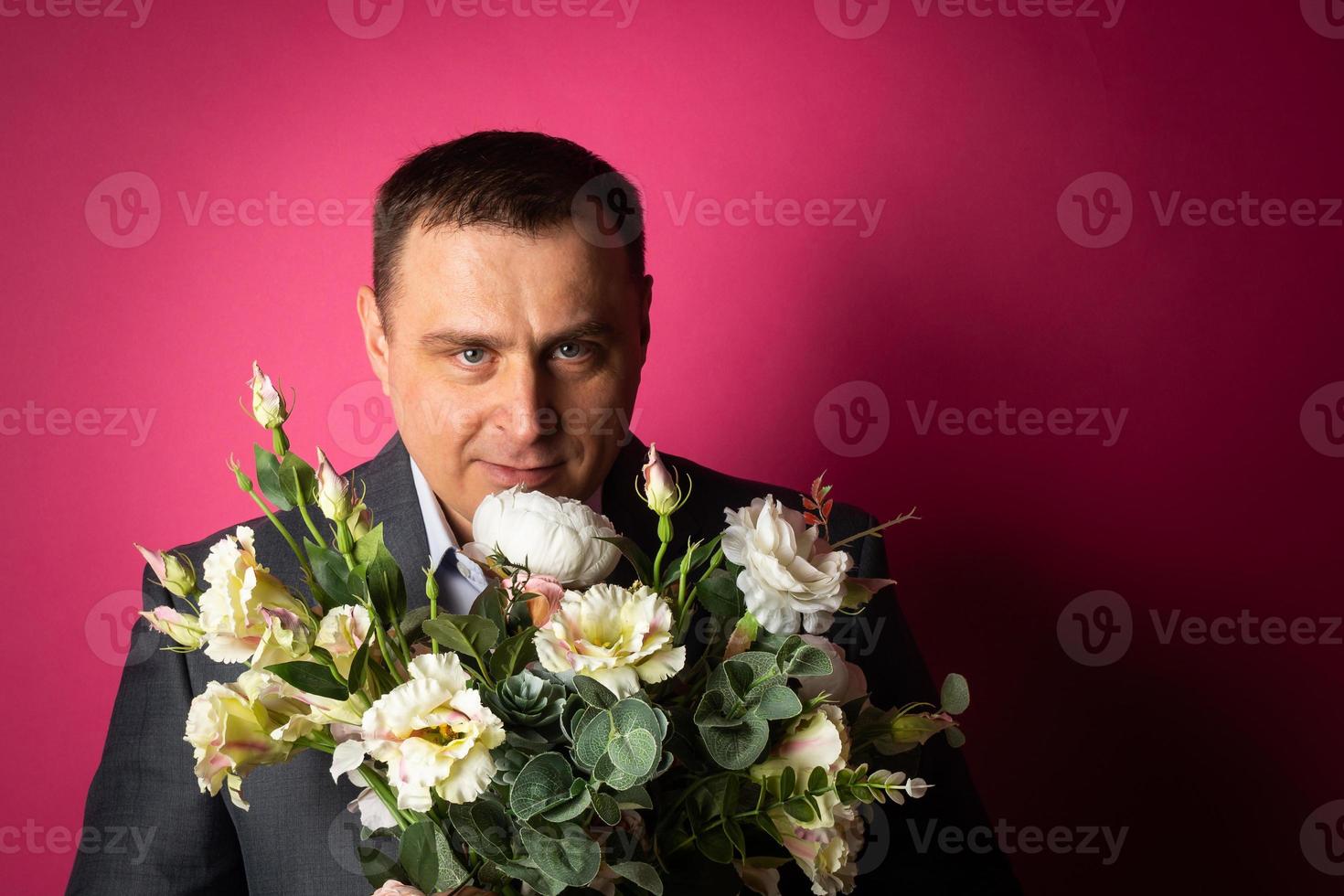 knap zakenman in een pak looks Bij de camera met een boeket van bloemen. foto