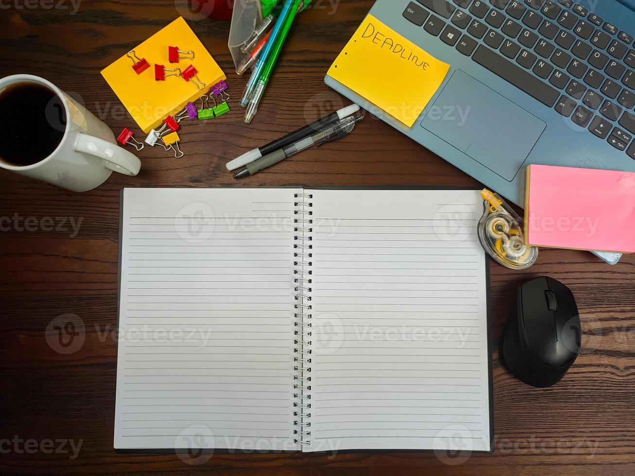 vlak leggen, een bespotten omhoog van een notebook. werkruimte in de achtergrond van de kantoor bureau van de top visie. met wit notitieboekjes, laptops, kantoor benodigdheden, potloden, en koffie cups in de houten bureau. foto